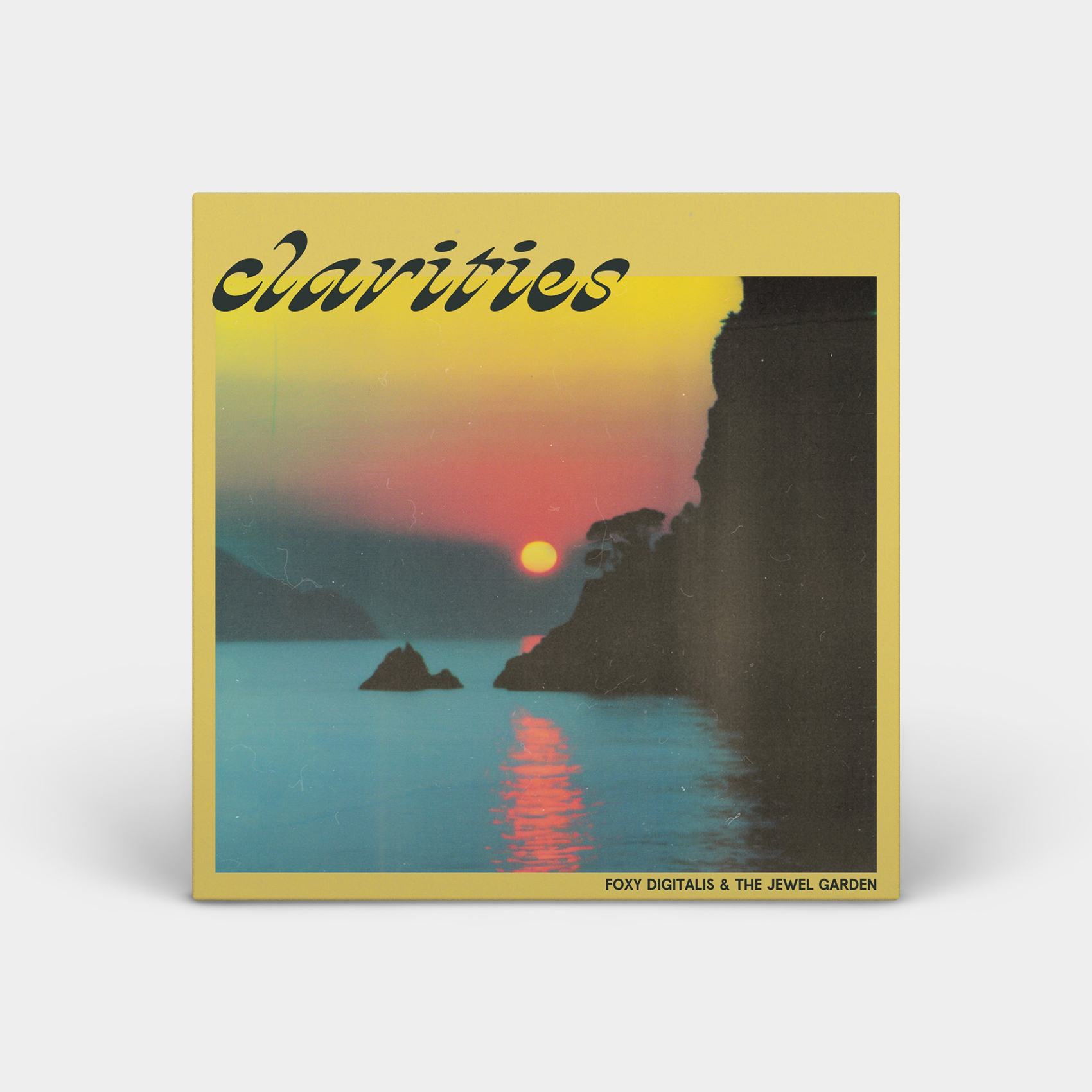 Album cover made to look 3d on a light grey background with shadows below it. The cover is yellow with photo of a sunset over water with a cliff wall in shadow on the right. The sunset is pink and yellow and the sun is reflecting orange/pink in the water. Text in the upper right corner reads “Clarities’ and text on the bottom left reads “Foxy Digitalis & The Jewel Garden”.